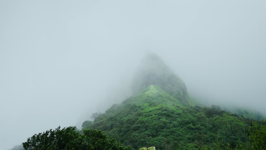 4K shot of clouds covering the Lohgad fort during the monsoon season near Lonavala in Maharashtra, India. Fog covers the fort on a cliff due to the moving clouds and rain in Monsoon season.