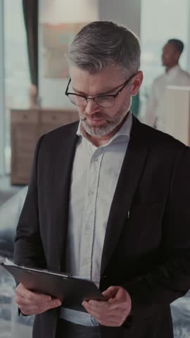 Portrait of Successful Confident Real Estate Agent with Documents inside Apartment. Cheerful African Married Couple Enjoying New House in Background.