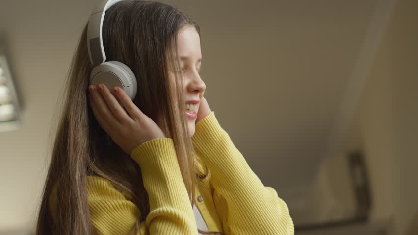 A close-up shows a person wearing a sunny yellow cardigan, a white top, and a patterned skirt, holding an indiscernible object. The indoor setting is cozy, with a bookshelf visible in the backdrop.