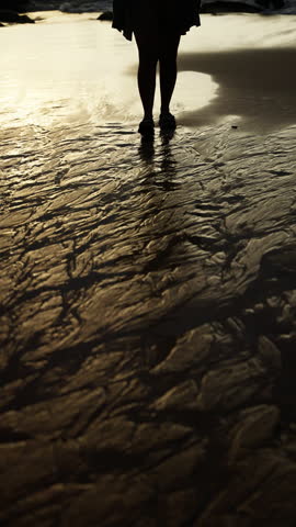 Silhouette of a Person Standing on a Textured Sandy Shoreline with Reflections During a Calm Sunset Creating a Dramatic and Peaceful Ambience