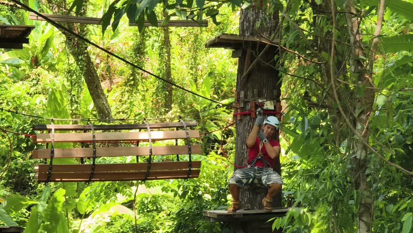 A man is enjoying an exhilarating ride on a zip line that traverses the thick woods surrounding him