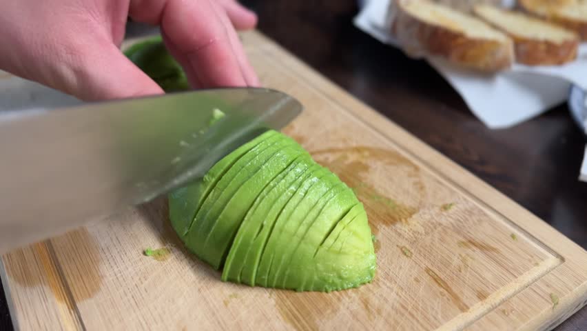 Close-up of peeled avocado being sliced with a knife on a bamboo cutting board. Fresh and ripe avocado texture shown clearly, perfect for cooking or healthy food content.