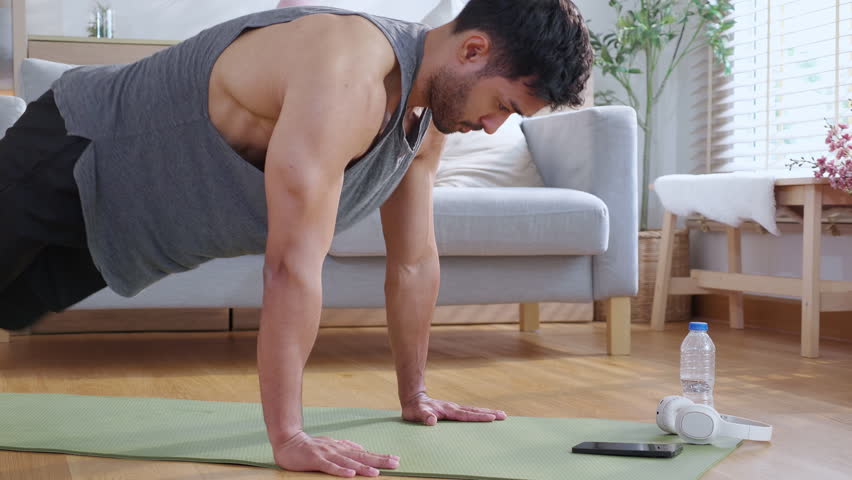 Young asian man doing pushup exercise in living room at home with determination, man training on yoga mat, bodybuilding strength and fitness for healthy lifestyle, workout routine, self-care.