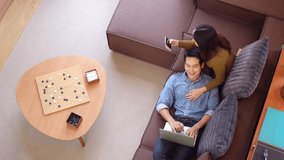 Bird eye perspective of adult asian couple home technology setup man reclines woman sits by him both using laptop showing an asian couple home technology everyday moment at residence. - Powered by Shutterstock - Get 15% off with code: PIKWIZARD15
