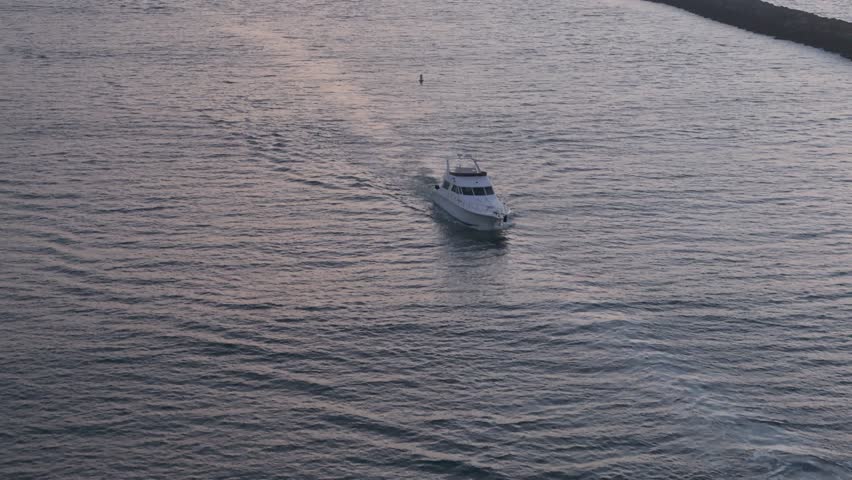 Telephoto aerial tracking shot of boats sailing through the Alamitos Bay Inlet at sunset, Seal Beach, California