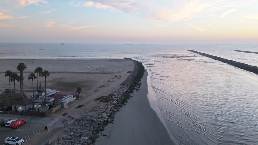 Aerial flyover of the San Gabriel River at sunset with waves crashing into the rocky jetties, Seal Beach, California