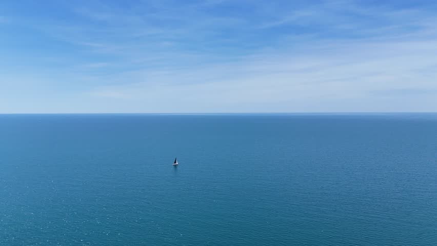 Lone Sailboat Floating in Vast Open Sea Under Serene Blue Sky