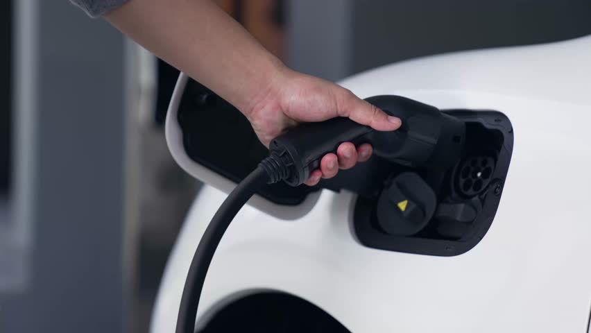 Man recharge his electric car with EV charger from smart home charging station display futuristic digital battery status hologram. EV car and home energy infrastructure for sustainable power. Peruse