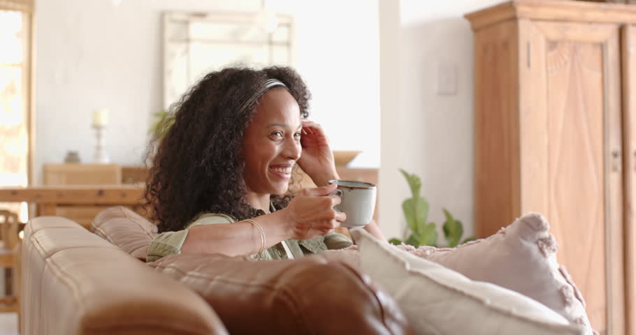 woman relaxing on sofa, enjoying coffee and smiling warmly, at home. Relaxation, leisure, cozy, contentment, home, lifestyle