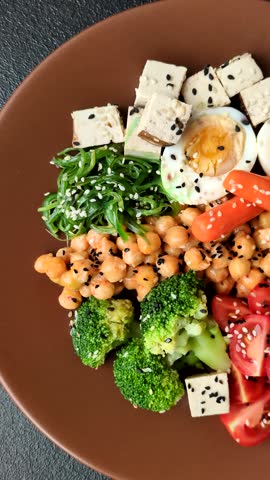 Vegan salad, bowls with chickpeas, broccoli, tomatoes, tofu cheese and boiled eggs. Vegetarian meal with vegetables, seeds and grains