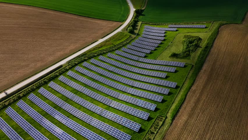 Drone footage of two cyclists riding along a rural road between grain fields and a large solar power station in Germany. A summer scene promoting healthy living and sustainable, green energy