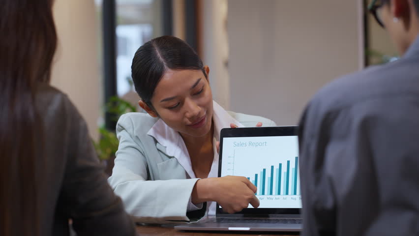 Confident asian businesswoman explaining growth chart on laptop screen during casual team meeting in modern cafe, female entrepreneur presenting business report to staff, small business strategy.
