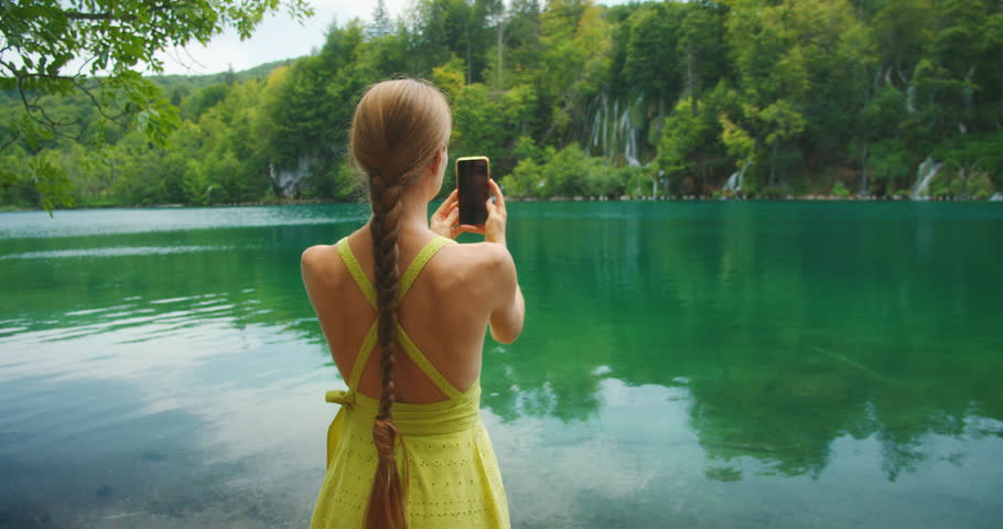Woman photographs nature with phone at Plitvice Lakes surrounded by green hills