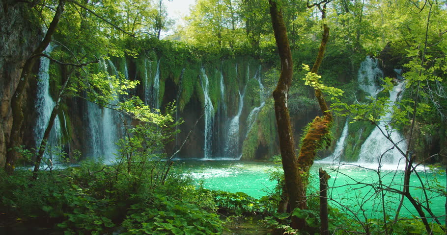 Waterfalls cascade into vibrant green lake surrounded by forest in Plitvice Croatia
