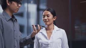 Young Asian businesswoman smiles while talking to a voice-controlled assistant app on a smartphone, held by her colleague. Concept of modern technology, teamwork, and digital lifestyle. - Powered by Shutterstock - Get 15% off with code: PIKWIZARD15