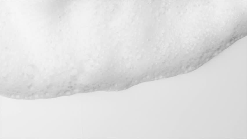 Foam bubbles background. Moving Soap foam popping bubble, white backdrop. Soap sud macro structure. Soap foam close-up. Clean, cleaning concept, laundry, shower. Slow motion. 