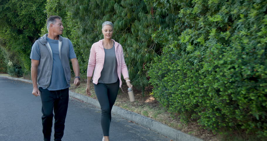 Mature couple walking outdoors, enjoying morning exercise in peaceful neighborhood, copy space. Fitness, wellness, active, lifestyle, togetherness