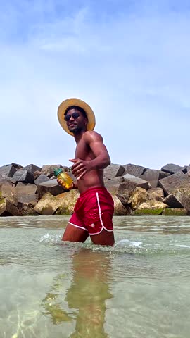 Joyful black traveler strolling through turquoise waters, sipping vibrant pineapple cocktail under bright sunlight, embodying carefree tropical vacation spirit