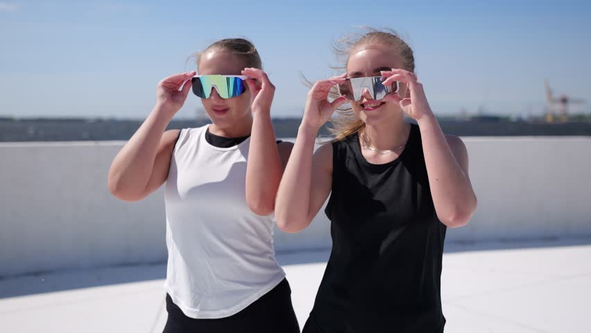 Dynamic duo showcasing stylish fitness wear on a sunny rooftop with vibrant blue skies and fluffy clouds