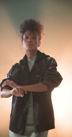 Vertical video: Confident woman in leather jacket posing with attitude in stylish studio. Fashion, style, trendy, urban, portrait, edgy