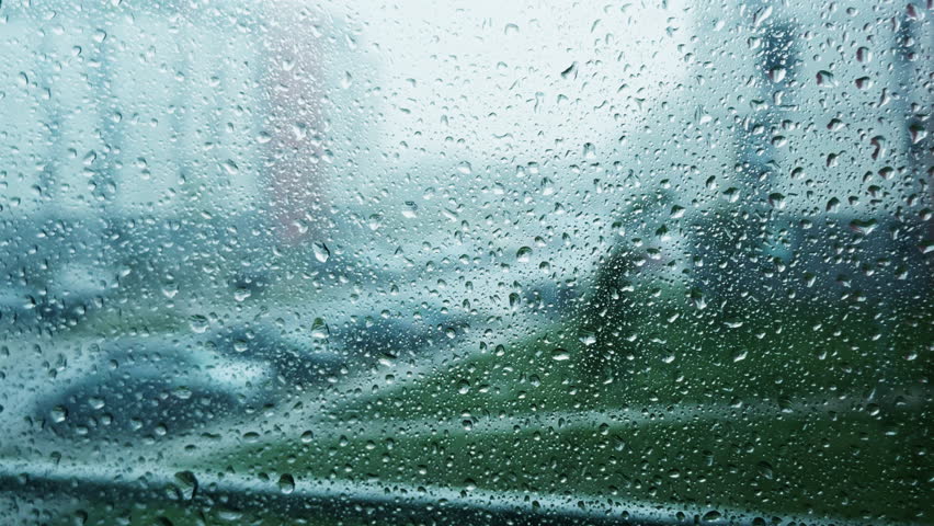 Rain pours heavily outdoors while water covers window glass with tiny droplets. Street view blurs as storm reduces visibility and adds atmosphere