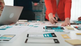 A dynamic group of professionals engages in a creative meeting, discussing user interface design concepts while utilizing digital devices and traditional paper tools. SACTR - Powered by Shutterstock - Get 15% off with code: PIKWIZARD15