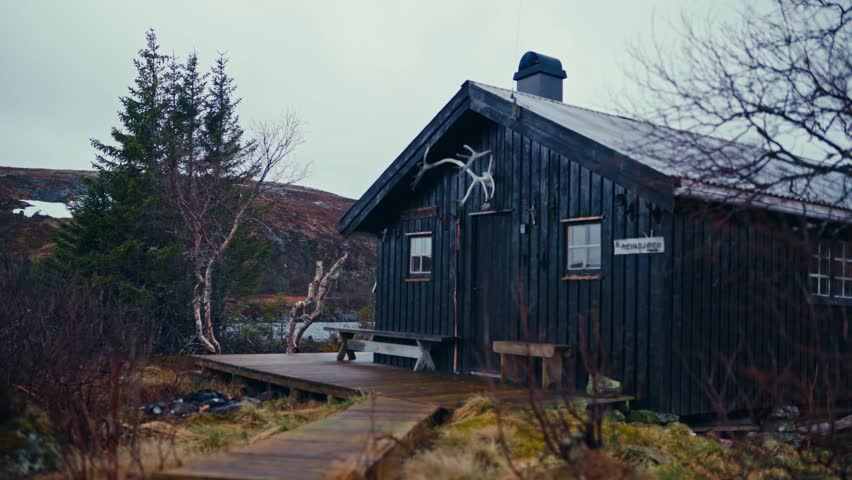 Man Walking Towards The Wooden Cabin By The Lake And Mountain In The Early Morning. - static shot