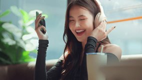 Happy asian woman using smartphone with wireless headphones at modern coffee shop, reusable cup on table – digital lifestyle, eco-conscious living and urban comfort - Powered by Shutterstock - Get 15% off with code: PIKWIZARD15