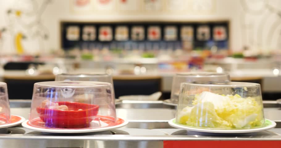 Sushi plates gliding along restaurant conveyor belt, transparent domes covering colorful rolls, showcasing culinary variety for hungry diners