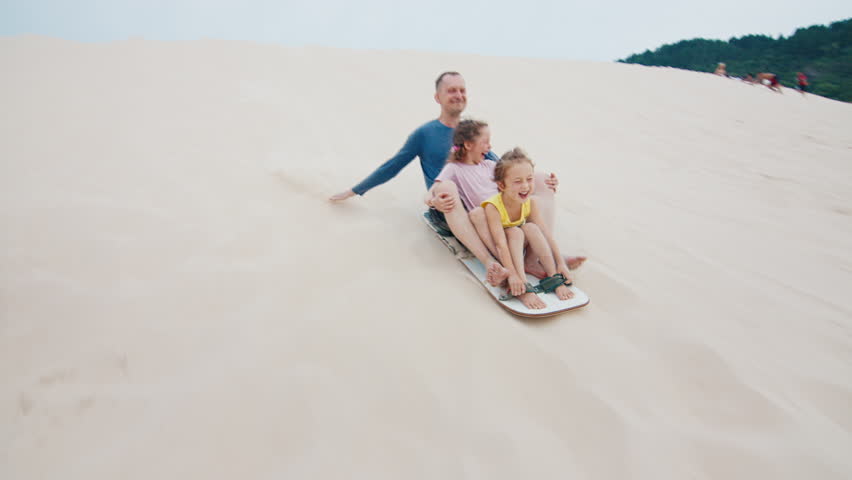 Family sandboarding. Man glides with girl down the sand dune with a lot of joy