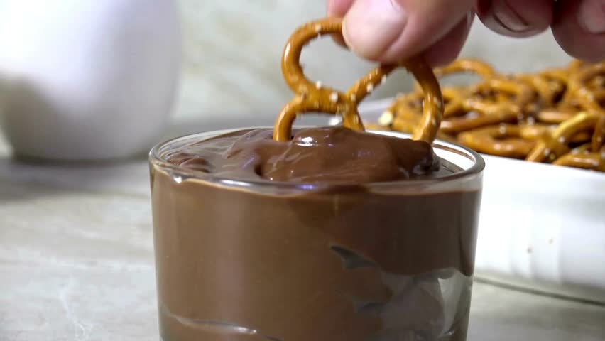 Hand Dipping a salted mini pretzel into melted milk chocolate sauce. Chocolate sauce and salted pretzels. Tasty mini pretzel with dark chocolate dipping sauce.