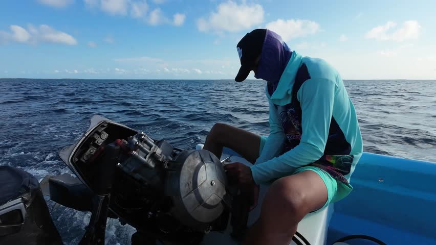 A young man opens the engine of a fishing boat while at sea to repair it.