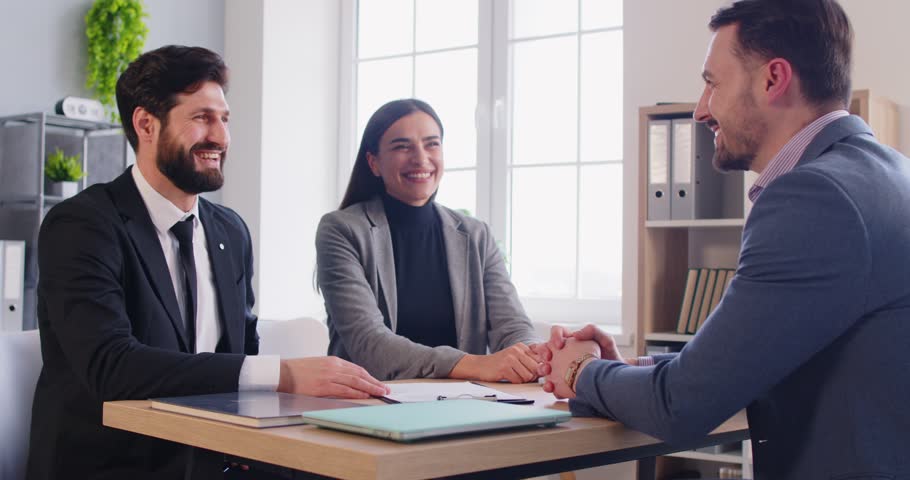 Happy couple shaking hands with business broker or insurance agent. Young man and woman having a good deal signing a contract with their investment adviser in office. 4k video. Slow motion.