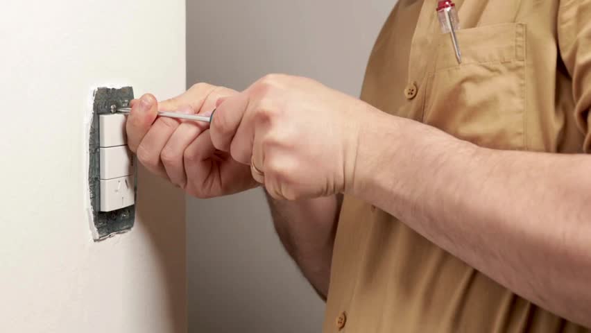 A skilled electrician carefully connects wires to a wall switch in a bright indoor environment, ensuring proper electrical functionality.