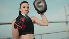 Close-up of a determined woman training in boxing, throwing a punch towards boxing pads held by a trainer outside. - Powered by Shutterstock - Get 15% off with code: PIKWIZARD15