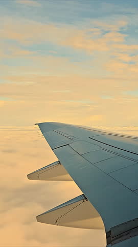 Airplane wing above clouds during golden hour, A serene view of an airplane wing slicing through clouds, captured during golden