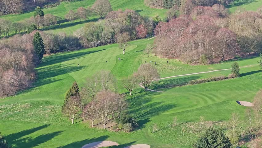 Aerial view of a stunning golf course in the countryside of Chesterfield, Derbyshire, England. A steep fairway with players walking the slope. Framed by autumn trees and greenery under a sunny day.