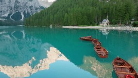 Slow panning drone shot over Lago di Braies at sunrise, gliding past traditional wooden boats as the calm water reflects the surrounding Dolomite peaks - Powered by Shutterstock - Get 15% off with code: PIKWIZARD15
