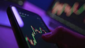 Close up, businessman using trading application on smartphone with stock market or cryptocurrency charts under neon lighting.Trader analyzing crypto trends on phone - Powered by Shutterstock - Get 15% off with code: PIKWIZARD15