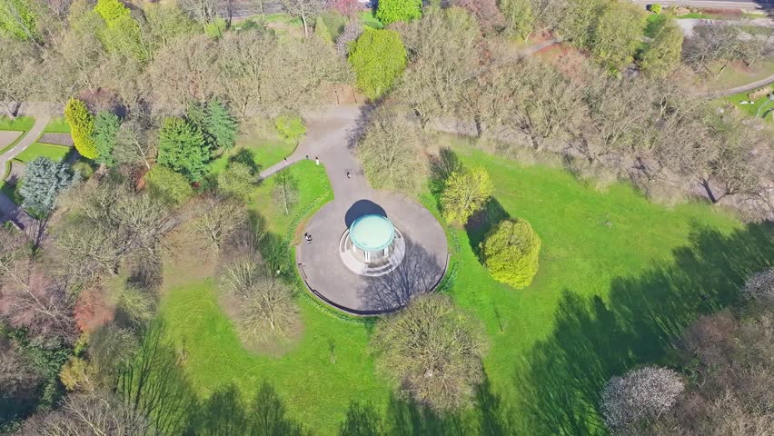 Aerial angled overview at open green field with gazebo at center of tree clusters in springtime urban park area Rotherham Clifton Park
