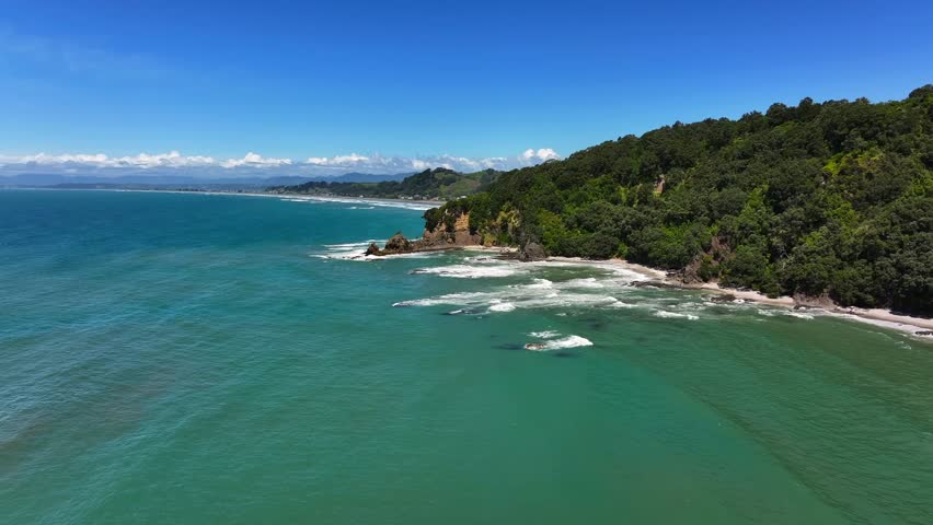 Summer Aerial beech Unspoilt jagged rocky coastline—turquoise waves crash against cliffs, windswept trees cling to edges, sunlight flickers across the wild, untouched shore. Drone New Zealand native