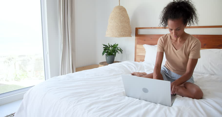 woman shopping online with laptop and credit card on bed, at home. Online shopping, e-commerce, technology, relaxation, bedroom, internet