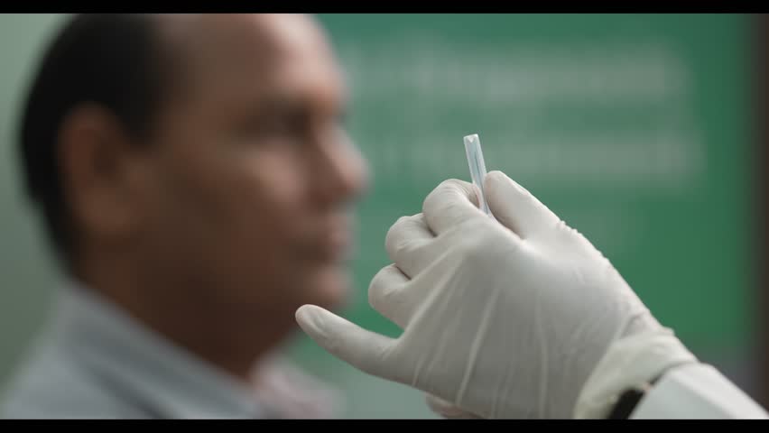 A close-up conceptual video of a nurse carefully opening the cap of a syringe, with a blurred male figure in the background. The scene emphasizes medical precision, patient care, and clinical readines