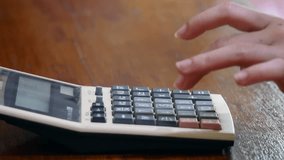 A hand pressing buttons on a vintage calculator with a wooden desk background, showing close-up details of keys and display - Powered by Shutterstock - Get 15% off with code: PIKWIZARD15