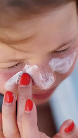 Close-up, the child, girls, severe sunburn on the face. Mom smears places of burns abundantly with a special cream. Mother applying sun protection cream to her daughter face