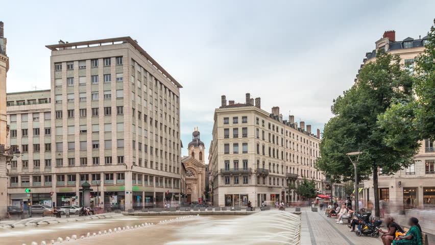 Hyperlapse of Place de la Republique in the historical center of Lyon, France. The square is dominated by a large fountain, surrounded by historic buildings, with people sitting on benches timelapse