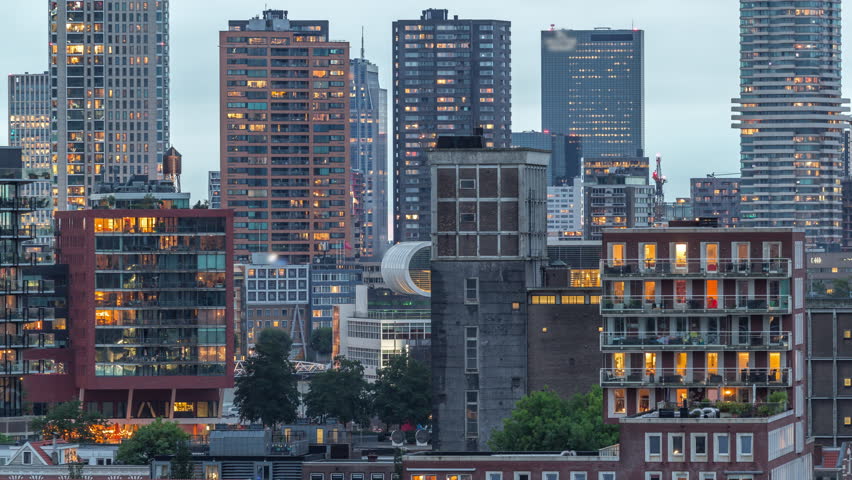 Aerial day to night transition timelapse of Katendrecht peninsula and Maashaven harbour in Rotterdam, The Netherlands. City skyline modern skyscrapers with glowing and blinking windows after sunset