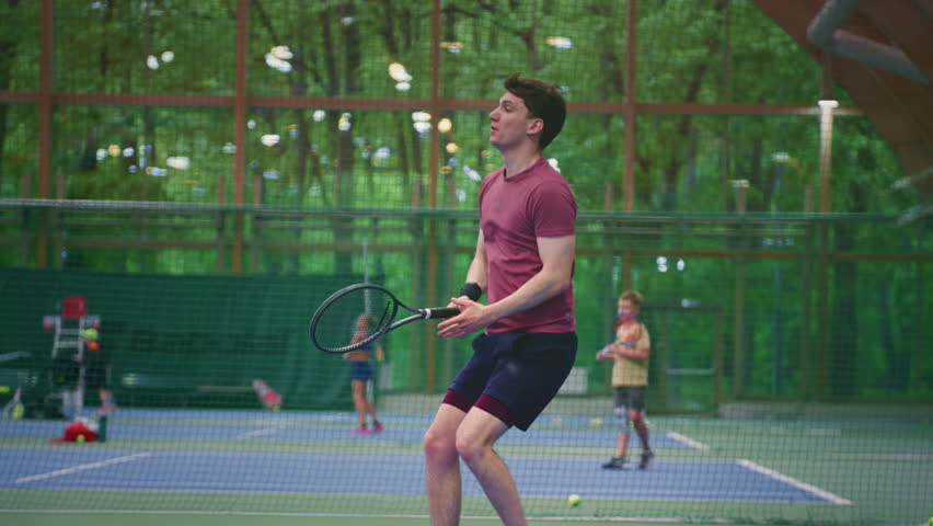 Man hits a tennis ball with a racket. Players in sportswear match or training workout game on indoor court. Healthy active lifestyle, fitness. Professional male hitting forehands strokes. Slow motion