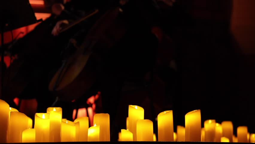 Musicians of an orchestra or ensemble performing surrounded by numerous lit candles. 