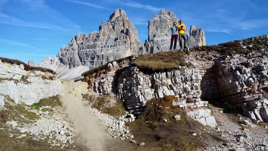 Aerial view of the beautiful Tre Cime di Lavaredo peaks. A man and a woman admire the breathtaking views of the surrounding landscape and the mountain range in South Tyrol, Dolomites, Italy.